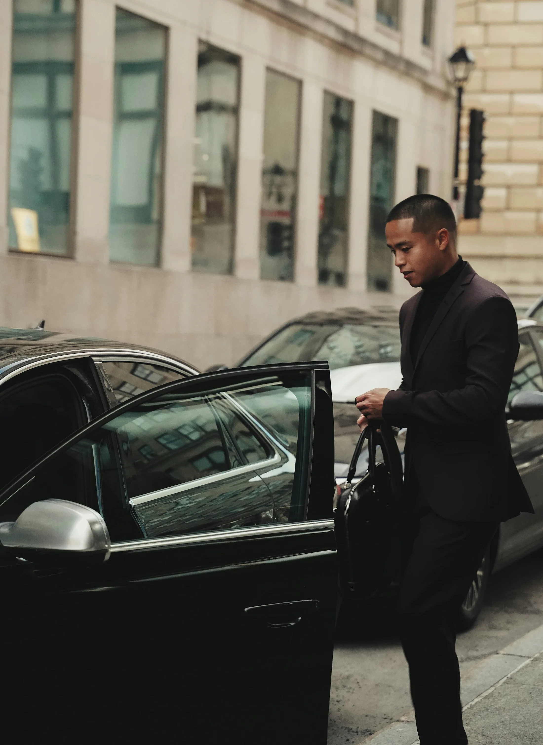 A uniformed chauffeur in a dark suit holding open the rear door of a luxury car