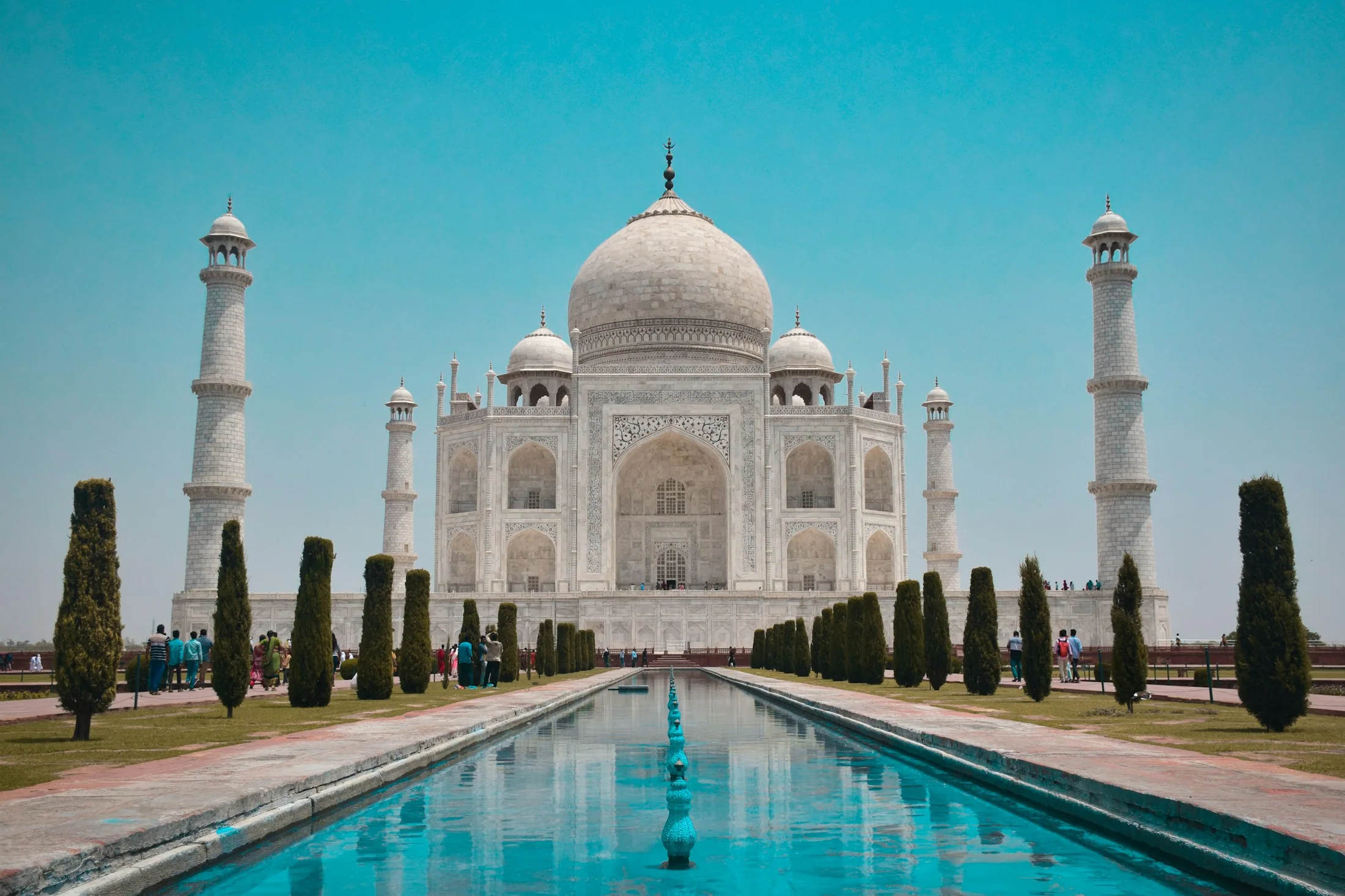 The Taj Mahal in white marble at the end of its reflecting pool, framed by dark cypresses