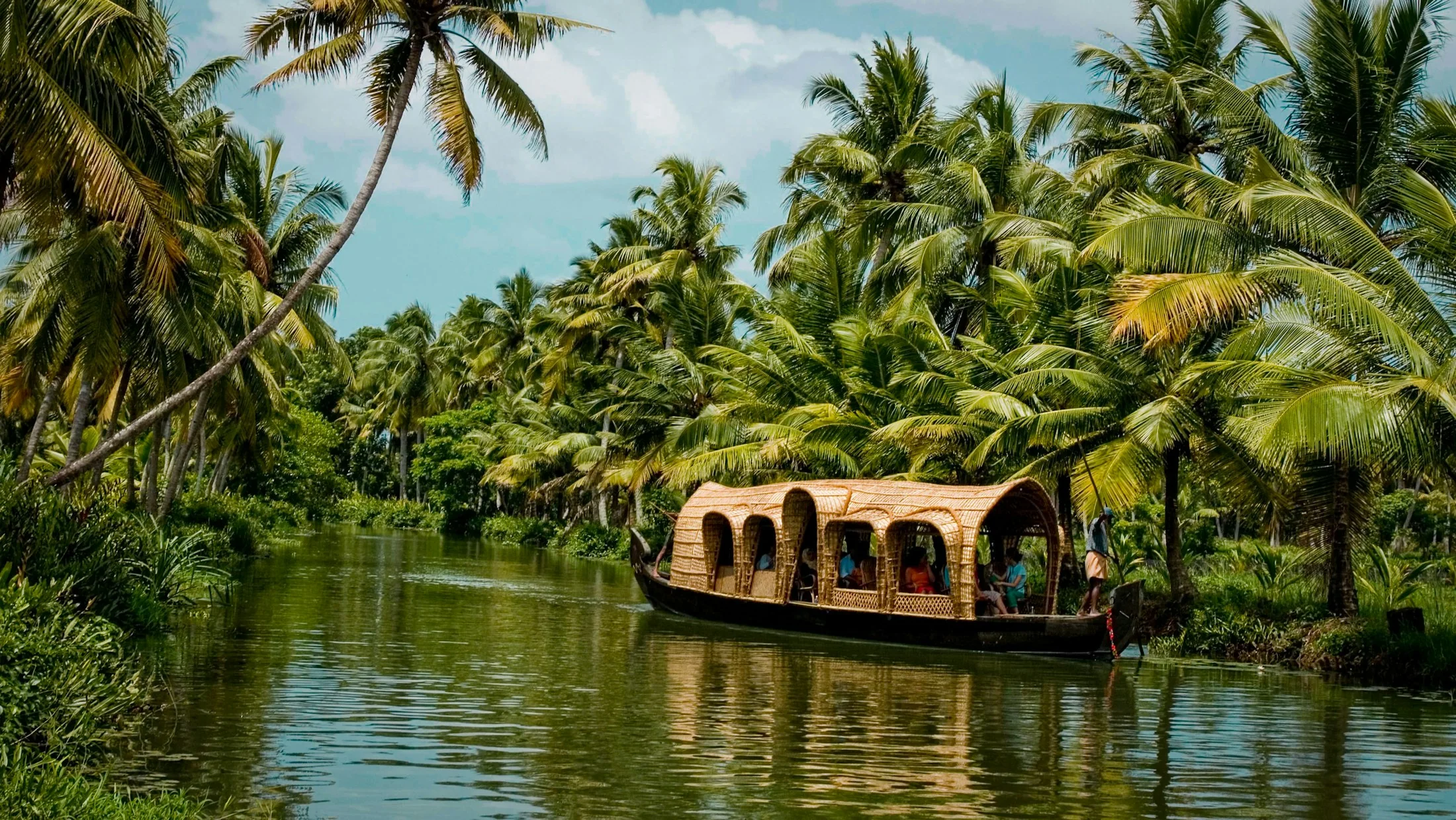 A thatched Kerala houseboat moored on a still backwater channel, coconut palms crowding both banks