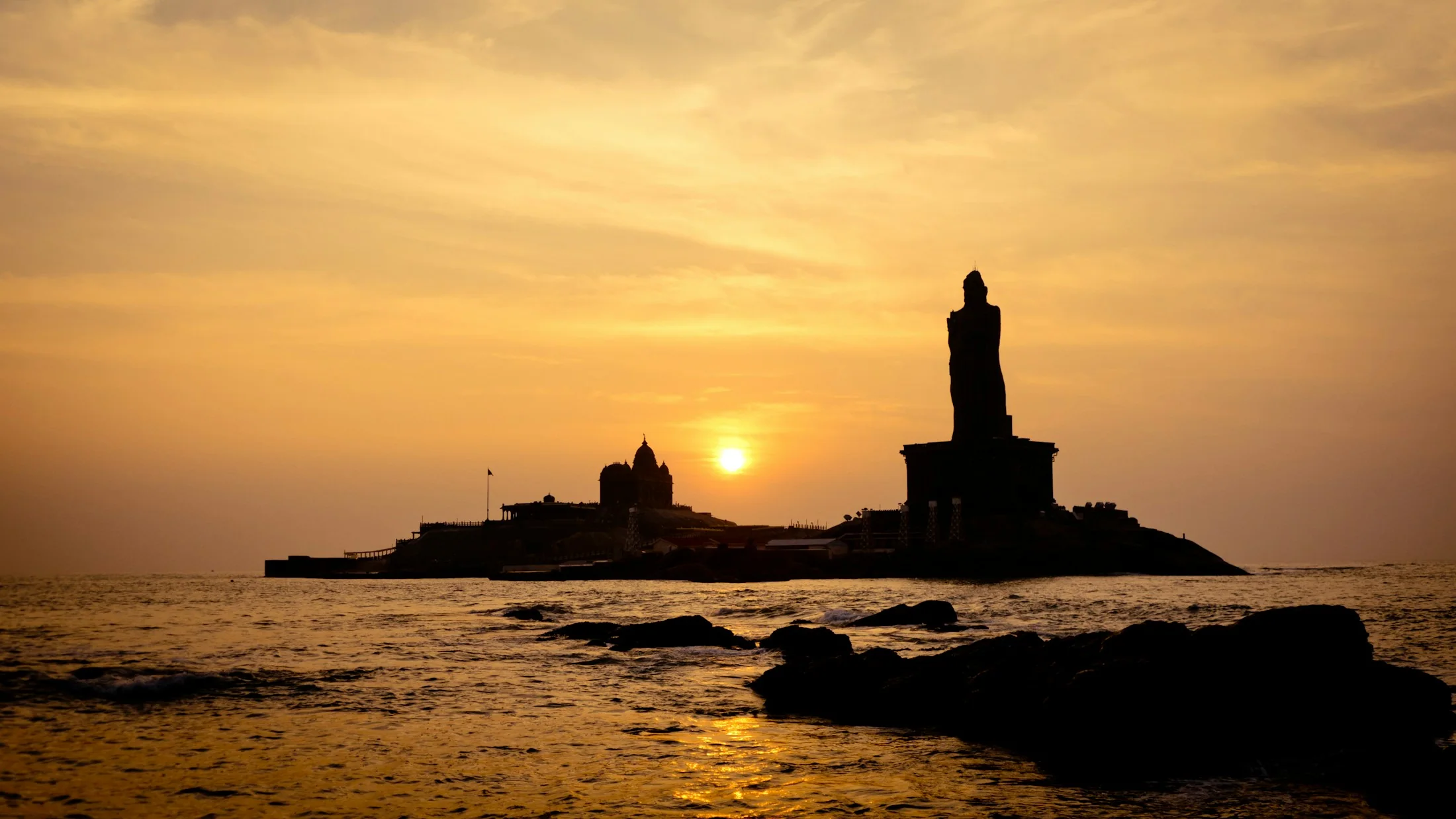 The Vivekananda Rock Memorial silhouetted on its offshore outcrop at Kanyakumari as the sun goes down over the water