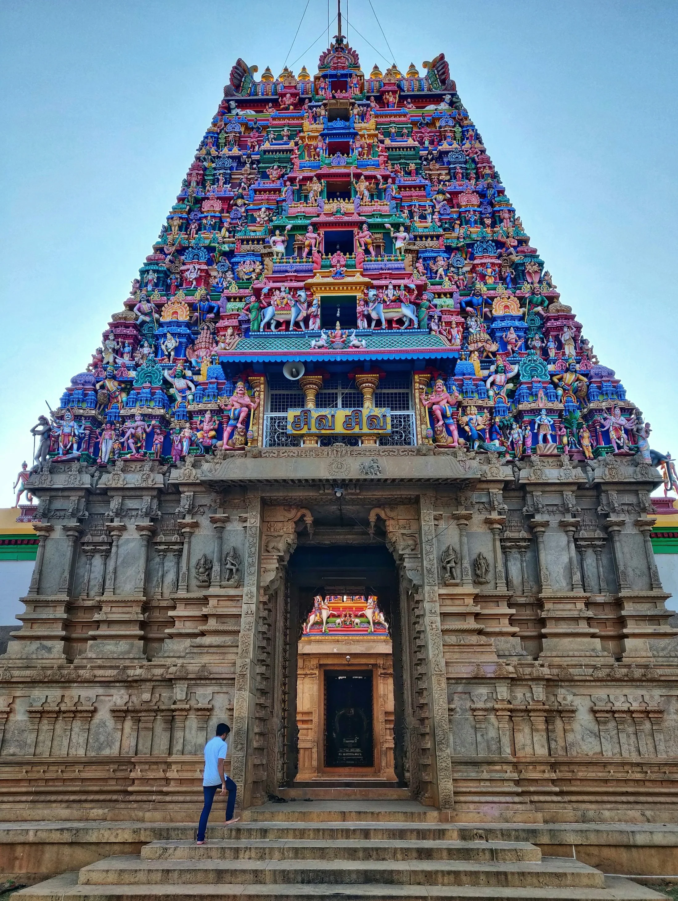 A guide standing at the foot of a towering sculpted temple gopuram, looking up at the tiers