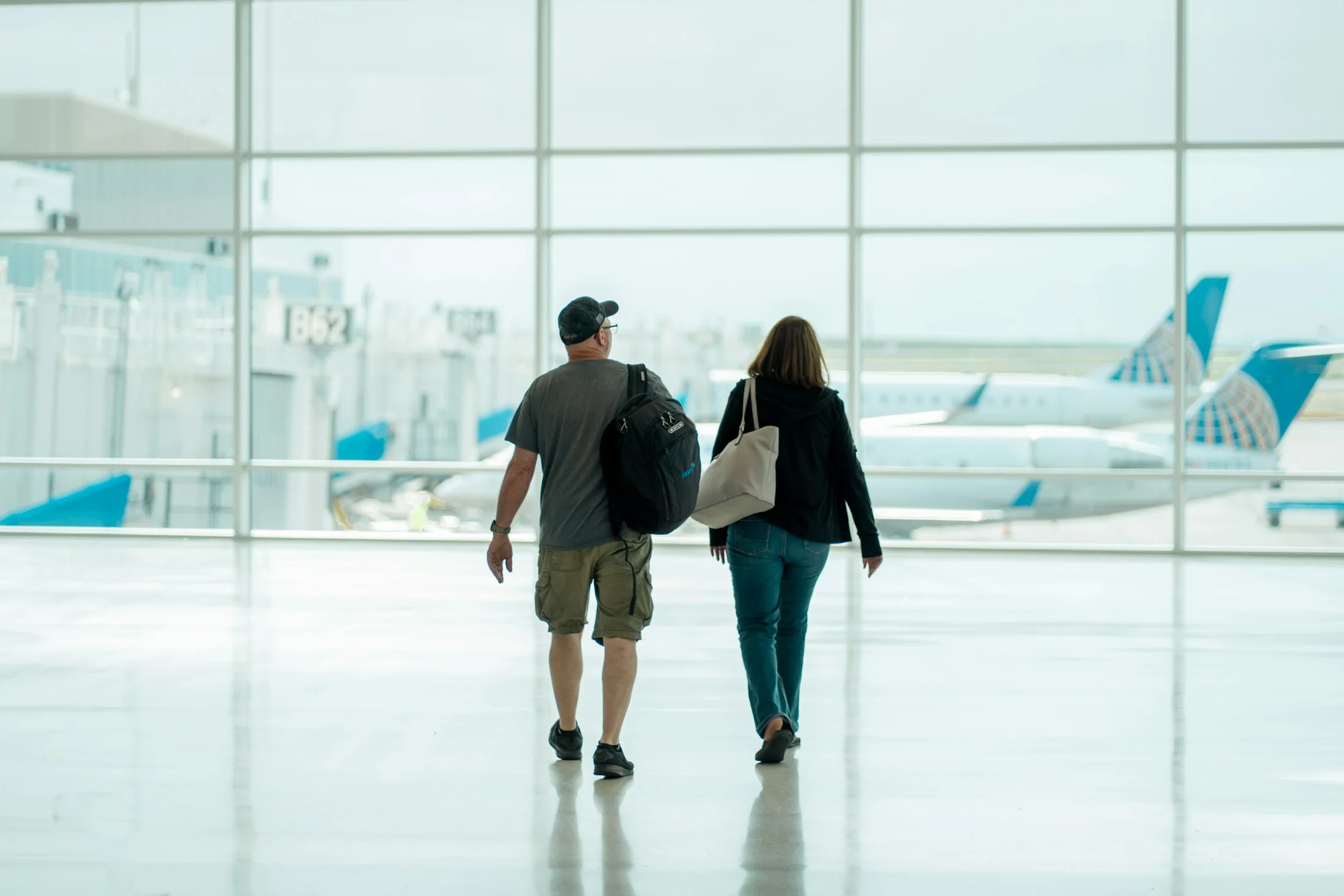 Two travellers walking through a bright airport terminal with an aircraft visible through the glass