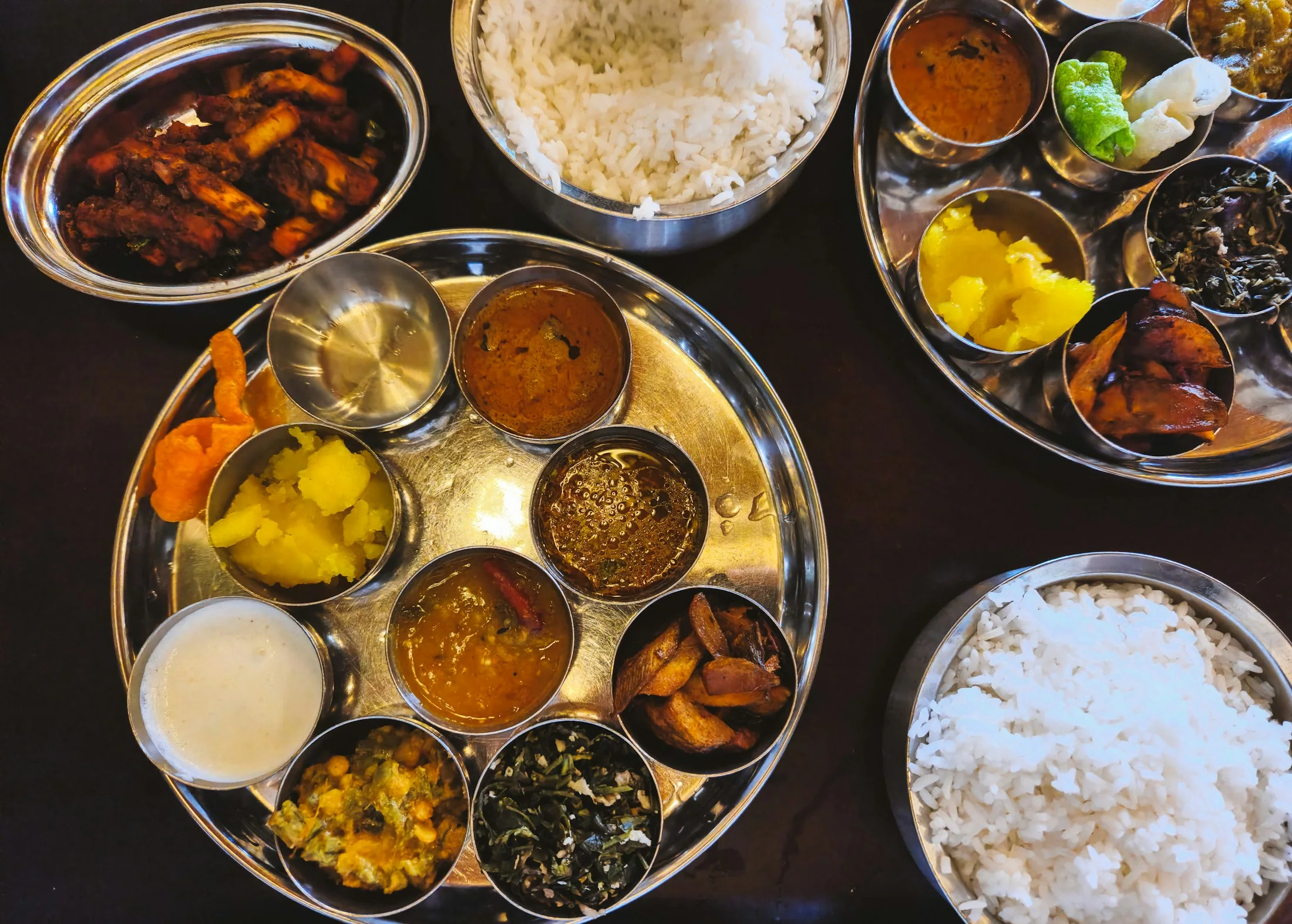 A South Indian thali laid out on a steel tray with rice at the centre and small bowls of curries, sambar and chutneys around it